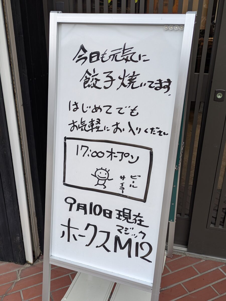 「今日も元気に 餃子焼いてます」「はじめてでもお気軽にお入りください」と書かれた、モモタロ店頭のホワイトボード。