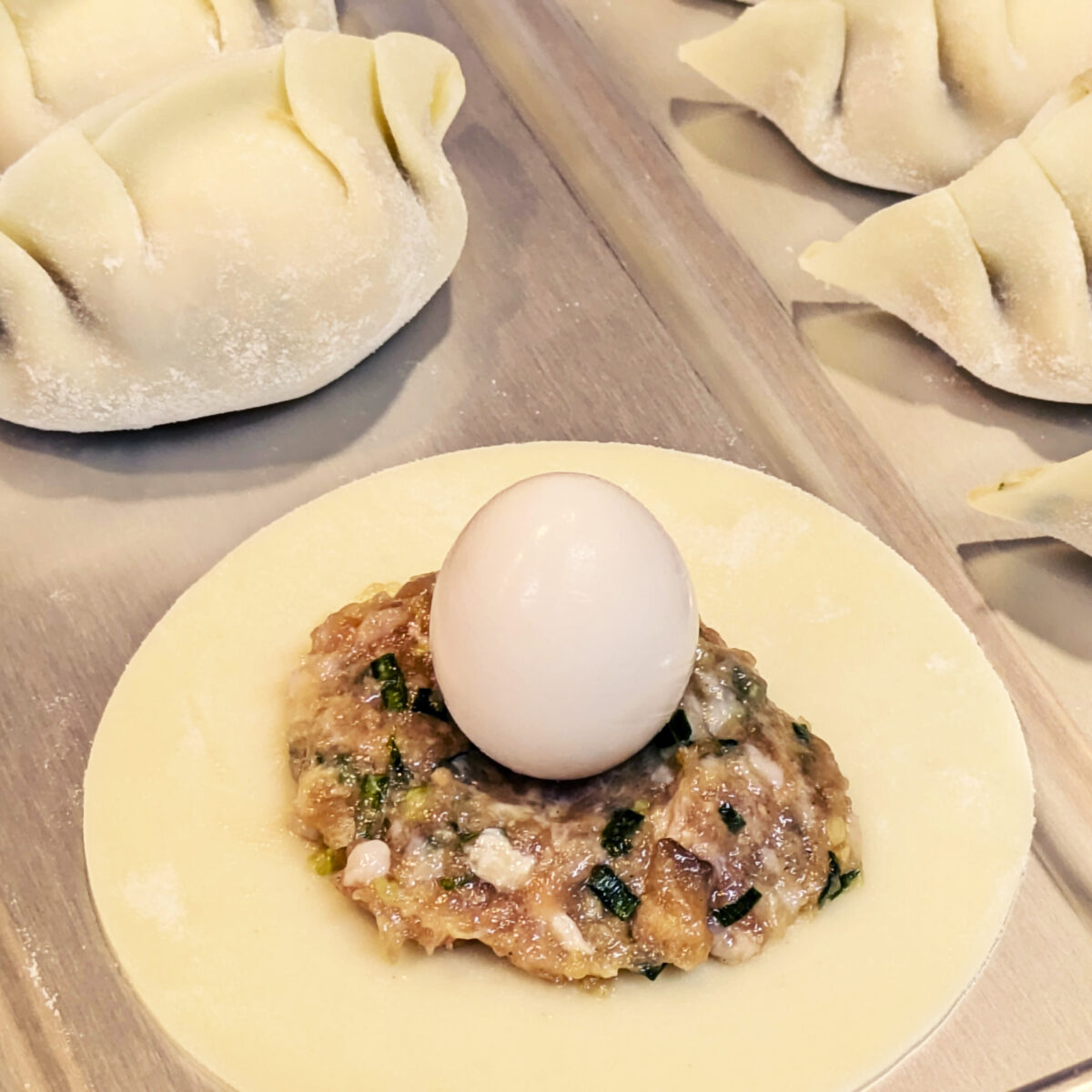 餃子の皮に広げた具の上に、うずら卵を丸ごと一つのせた仕込みの様子